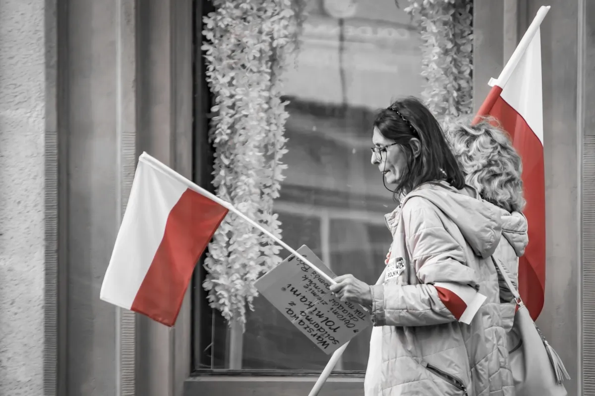 Woman carrying a Polish flag past reflective windows